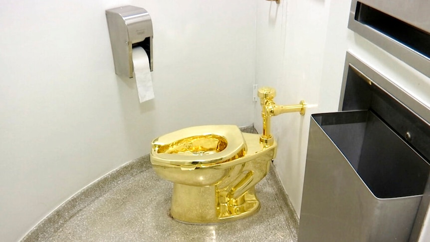 An 18-carat gold toilet is shown in a drab grey bathroom cubicle surrounded by stainless steel instruments.