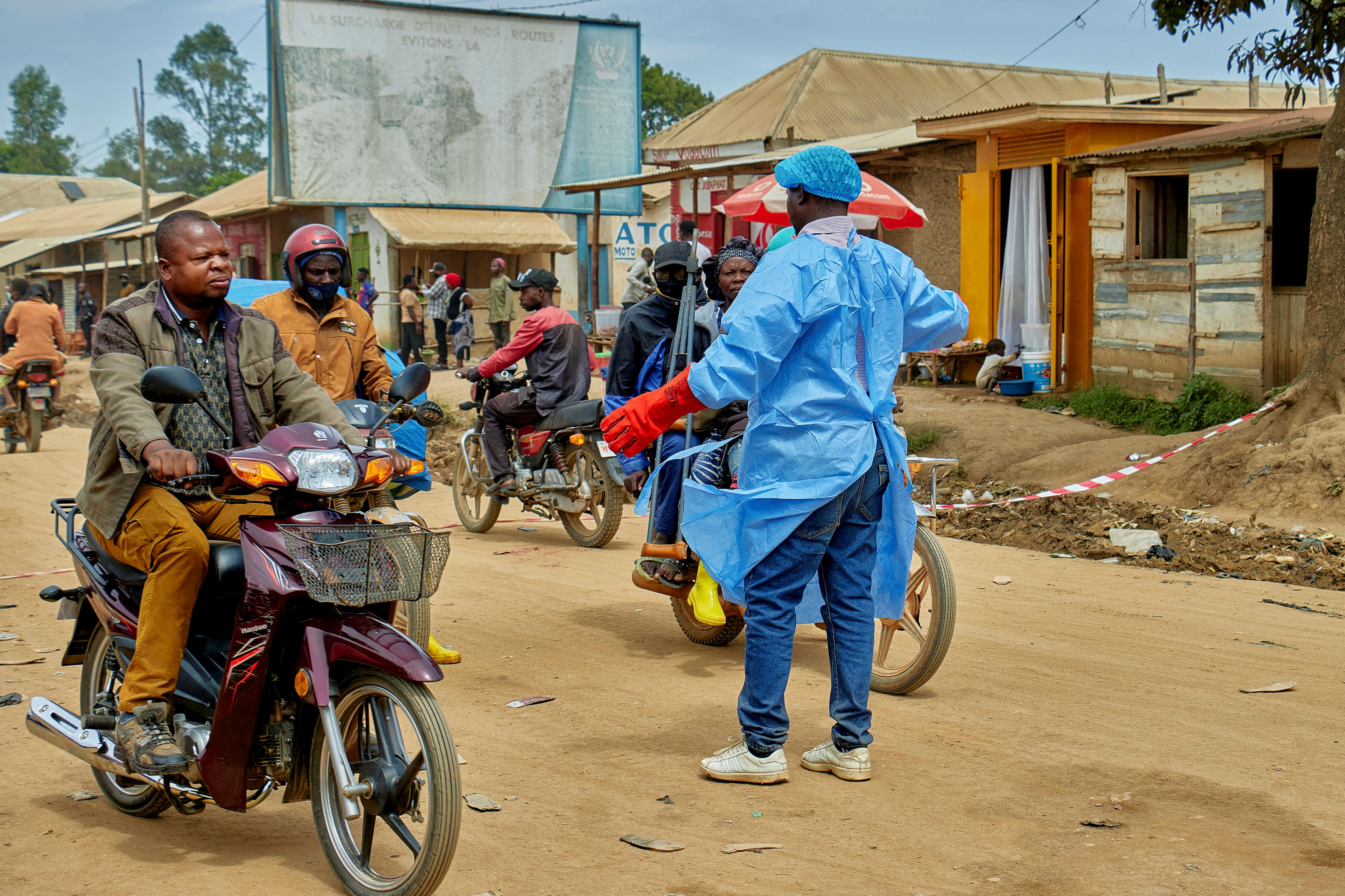 A man in blue protective gear stands in the middle of the street, blocking people on motorcycles.