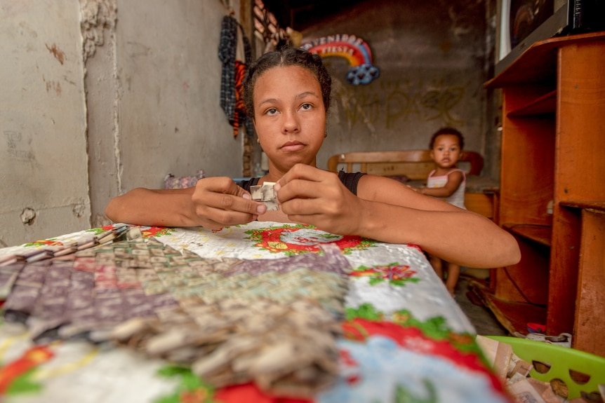 A serious looking teen girl weaving banknotes while a small girl looks on