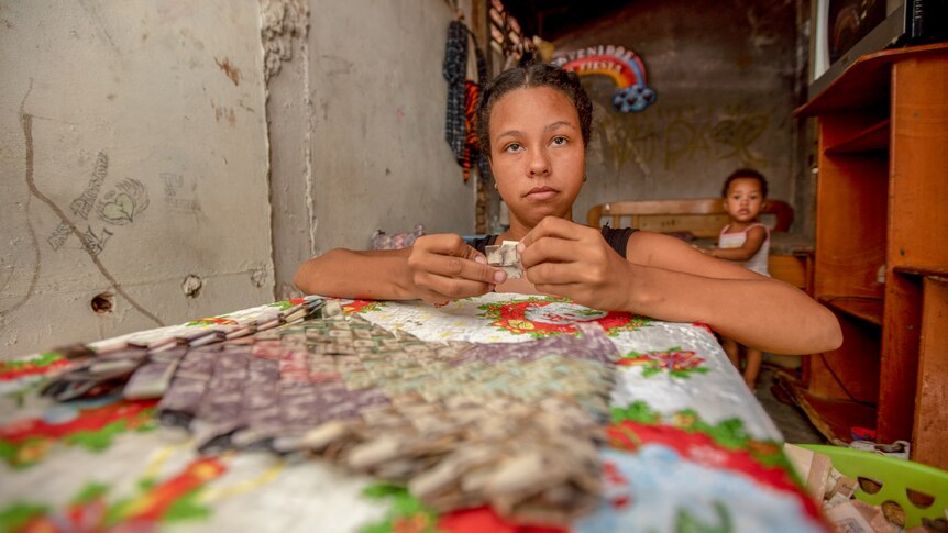 A serious looking teen girl weaving banknotes while a small girl looks on