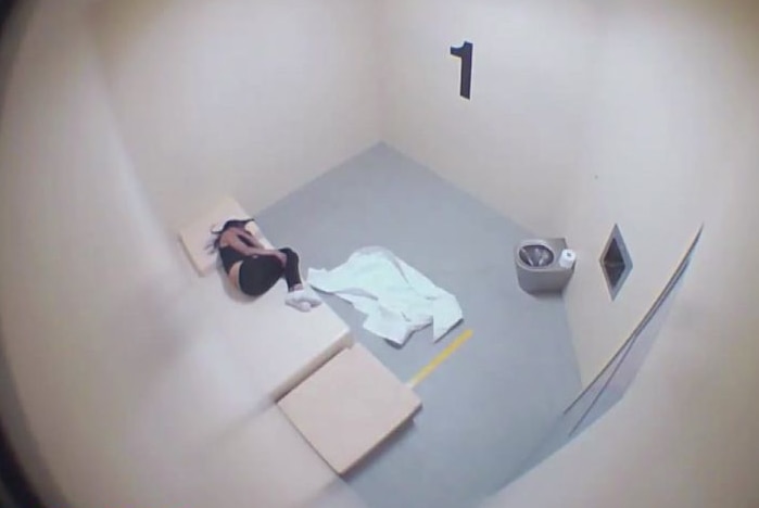 Woman lays on bed in a police cell.