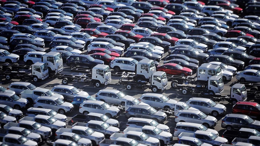 Scores of new car and truck imports, white, red and black,  parked on the wharf at the Port of Brisbane.