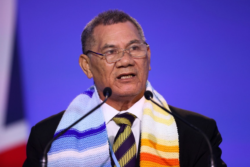 Man stands before microphone with blue and yellow scarf 