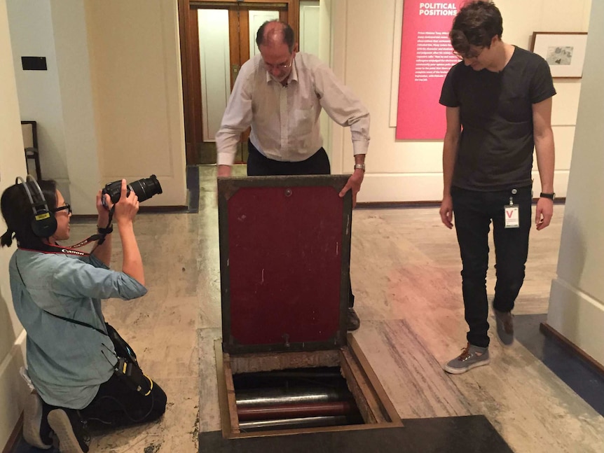 Sonya Gee holding a dsl camera as Michael Evans opens hatch to tunnel under Old Parliament House and Matthew Arnaudon watches.