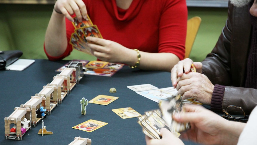 Closeup of a table where three people are holding and shuffling cards.