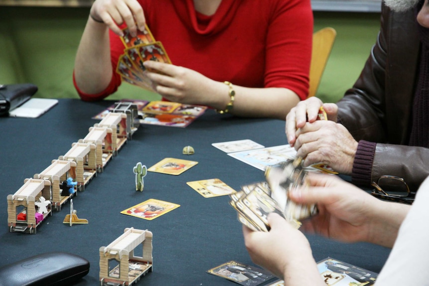 Closeup of a table where three people are holding and shuffling cards.