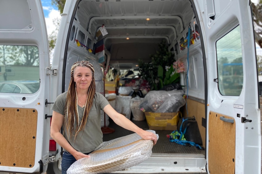 Une femme avec des dreadlocks debout à l'extérieur d'une camionnette avec un coffre ouvert.