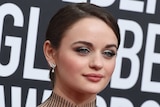 A close up for Joey King, wearing a dress with a high neck and lots of lines.
