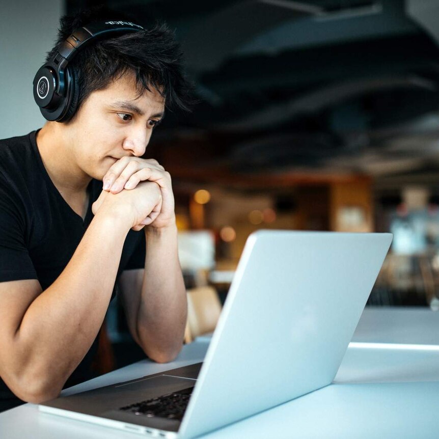 Male student with headphones on is looking into a laptop screen.