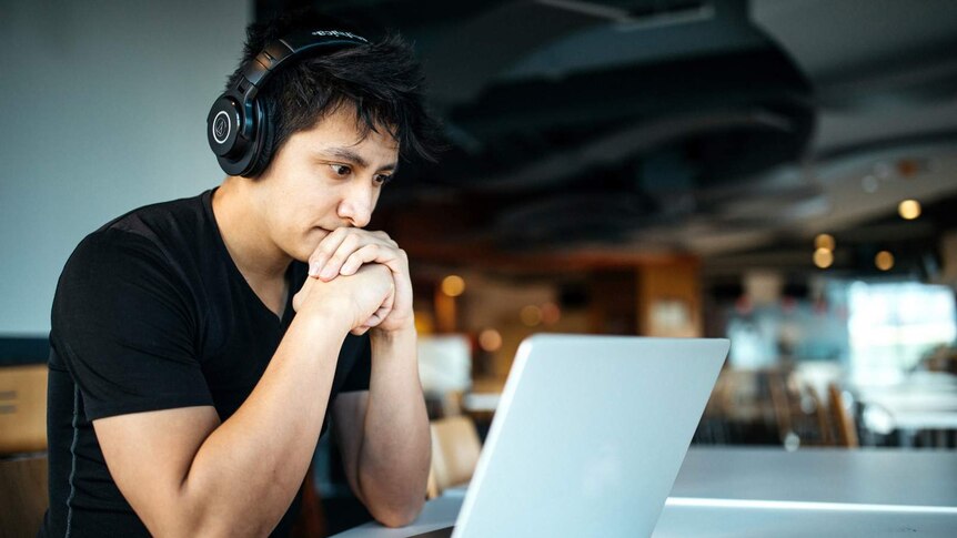 Male student with headphones on is looking into a laptop screen.