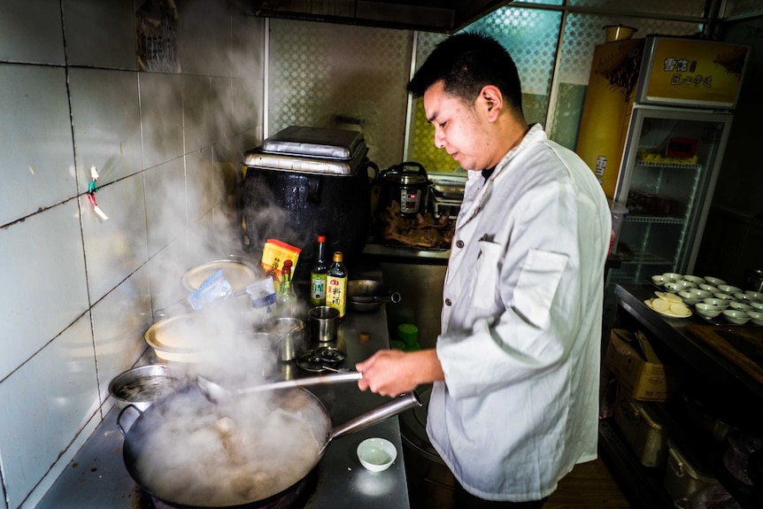 Wu Xianghai cooking dog meat in a wok at his restaurant in Guiyang.