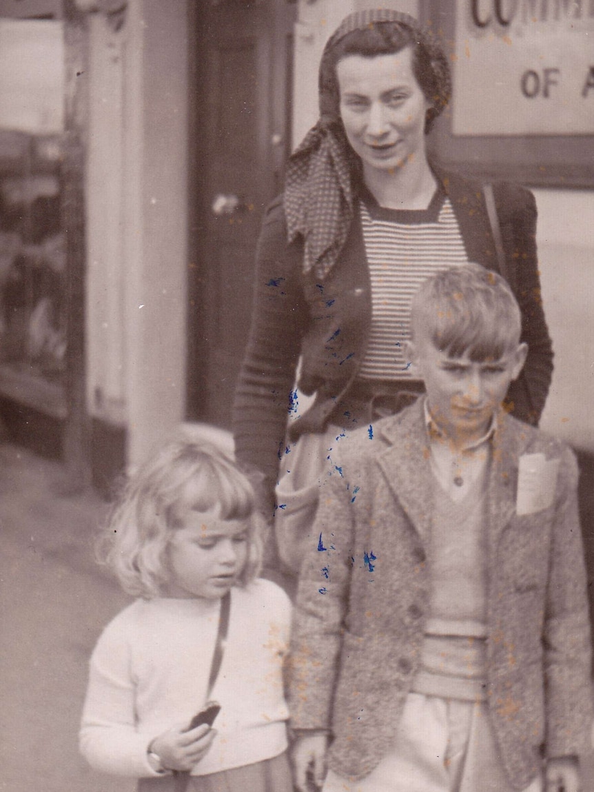 Lisellotte Wolf wears a head scarf and stands behind her young children in a black and white, scuffed photo.
