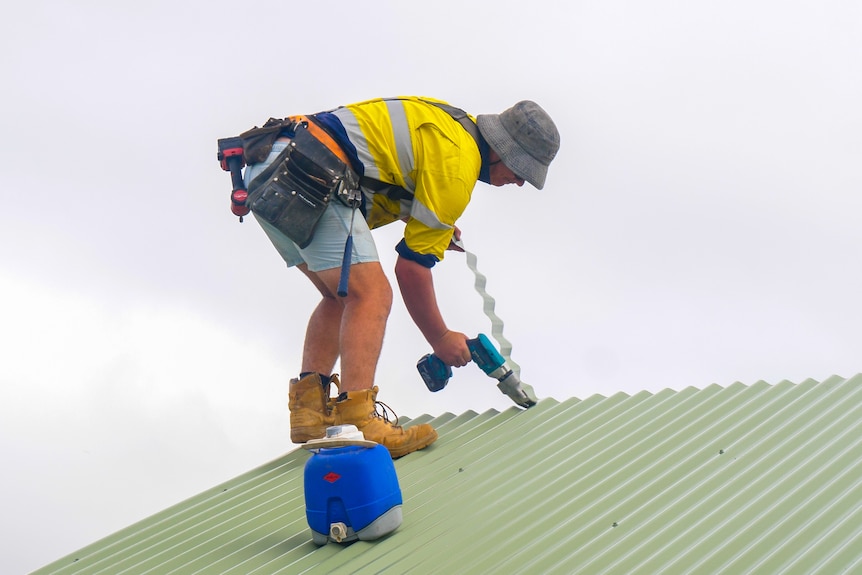 Un constructeur réparant un toit avec une perceuse