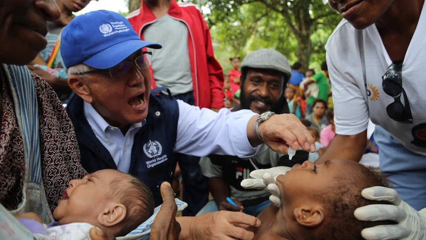 A health official gives a young person a vaccine via liquid drops into their mouth.