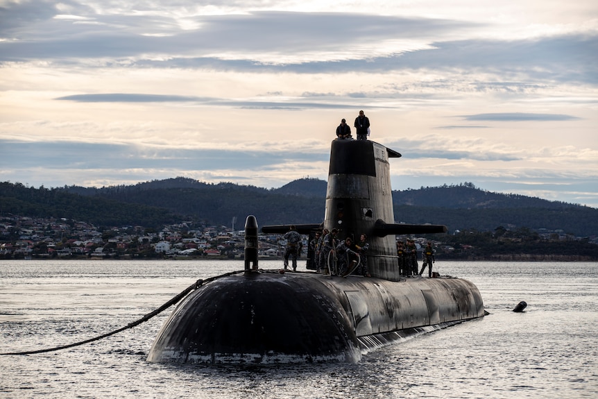 Crew stand on the top of a submarine as it's in the water.