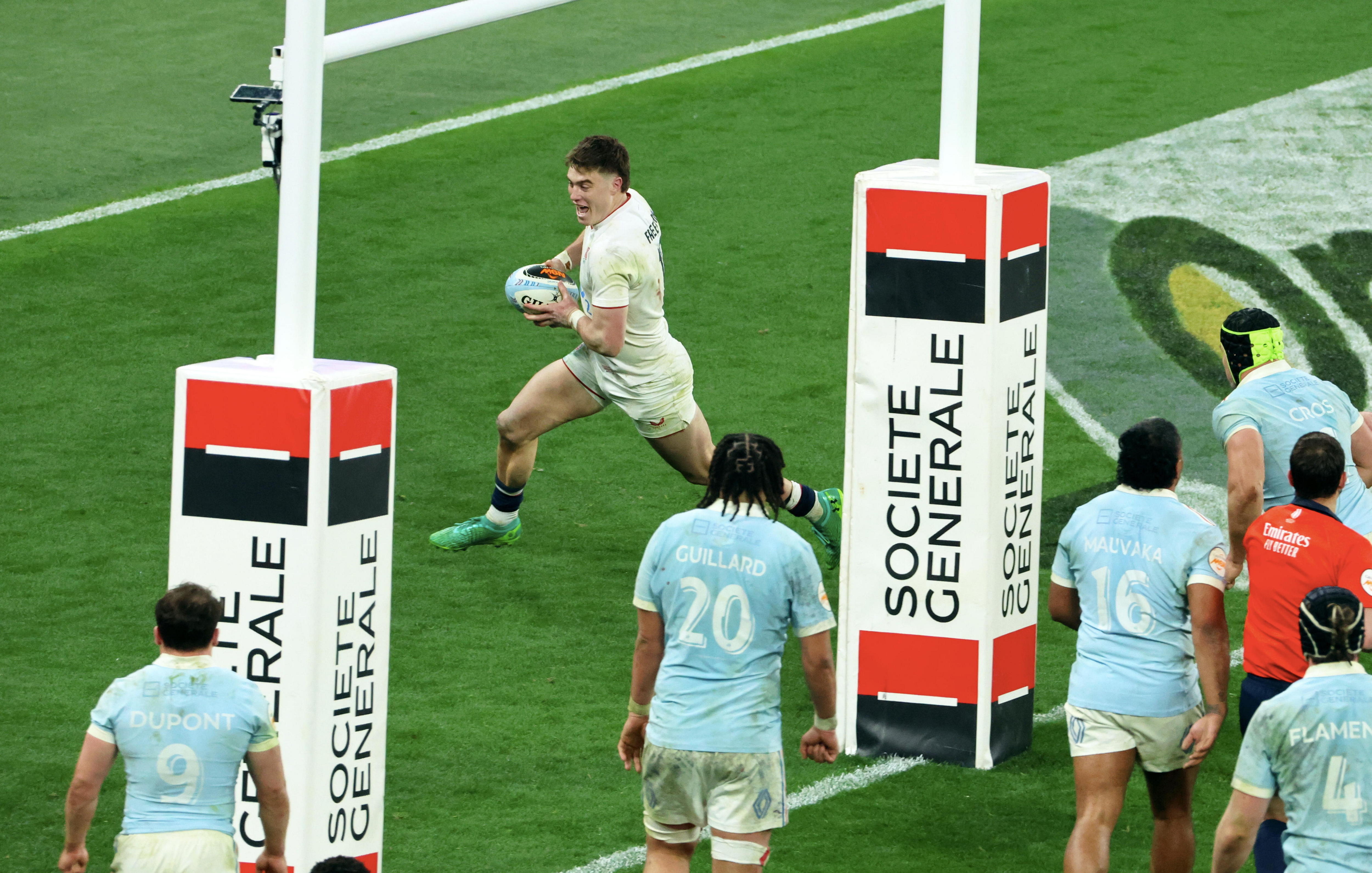 Um entusiasmado internacional inglês da união de rúgbi corre atrás dos postes para marcar um try enquanto a defesa francesa assiste.