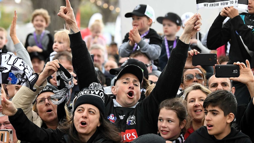 A crowd of Collingwood fans cheer and raise their hands at the AFL grand final parade.