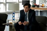 A still from the TV series Succession of a tall man in his early 30s in a suit sitting in an office, phone in hand, worried face