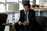 A still from the TV series Succession of a tall man in his early 30s in a suit sitting in an office, phone in hand, worried face