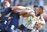 A Brumbies Super Rugby Pacific player holds the ball as he is tackled by Highlanders' players.