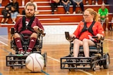 A man and a woman in electric wheelchairs battle for the ball with crowd in the background