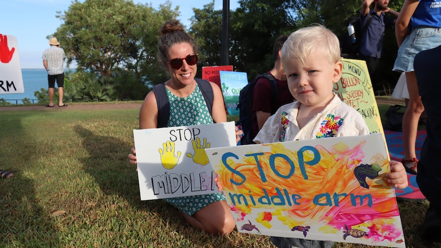 a young mum with her toddler holding signs warning against the middle arm project