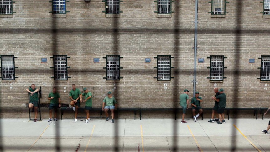Looking down through metal mesh, inmates stand talking in the prison courtyard.