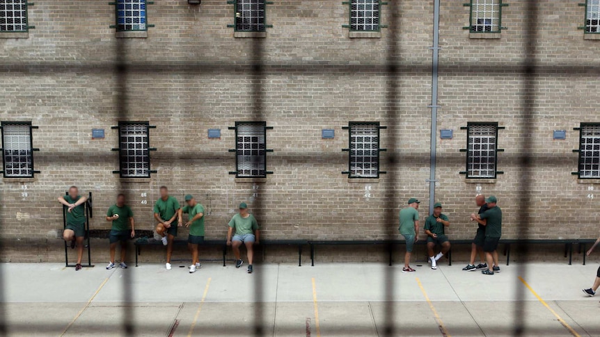 Looking down through metal mesh, inmates stand talking in the prison courtyard.