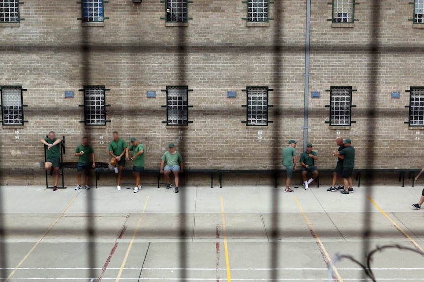 Looking down through metal mesh, inmates stand talking in the prison courtyard.