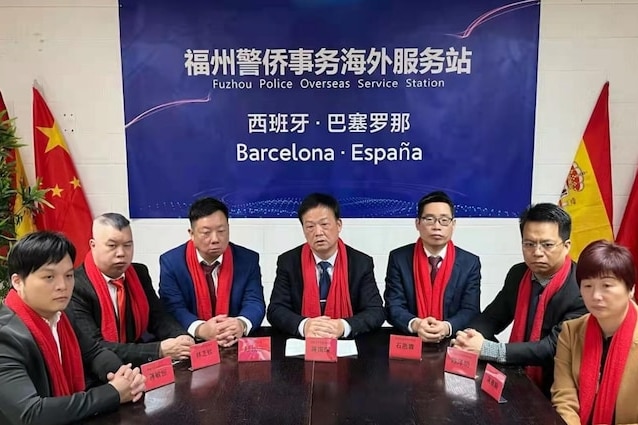 Imagine cu chinezi așezați în fața unui banner
