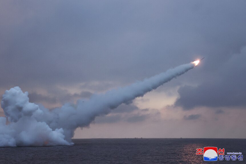 A small rocket launches off from the ocean with dark clouds in the background
