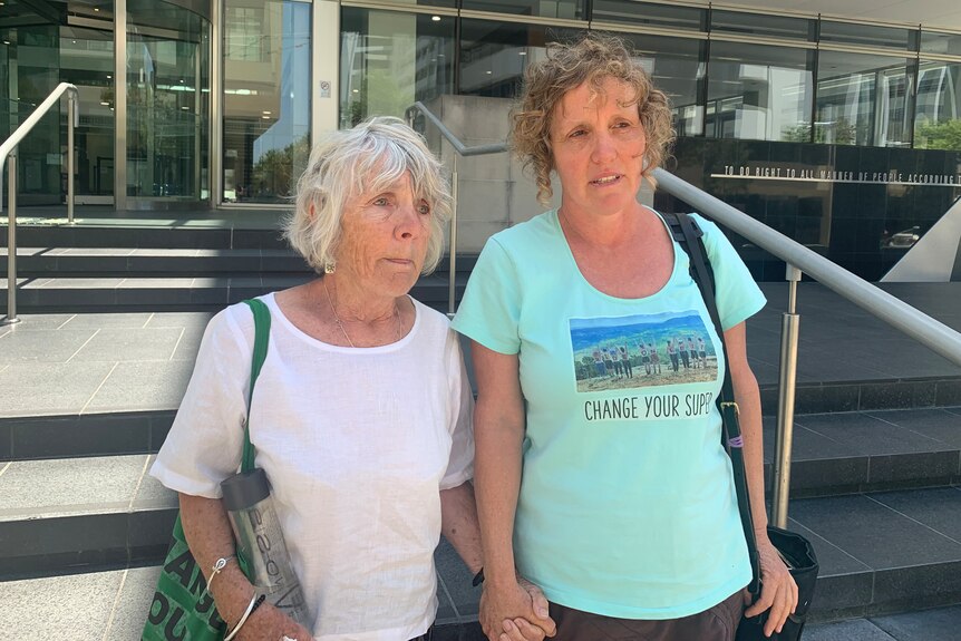 Two women stand outside court with serious looks on their faces.