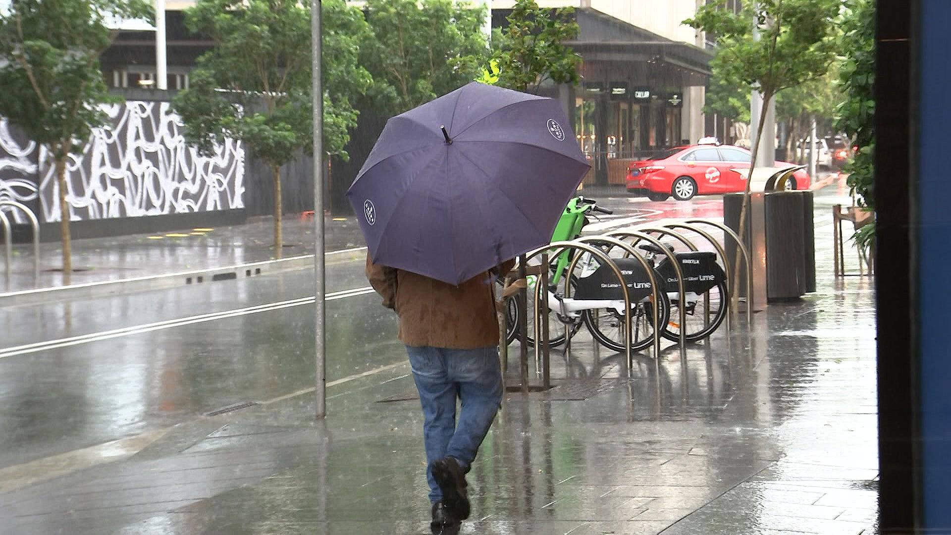 a man carrying an umbrella walking along a sydney street on a rainy stormy day