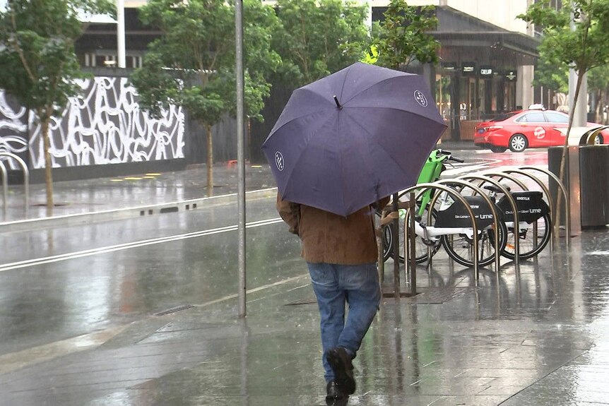 a man carrying an umbrella walking along a sydney street on a rainy stormy day
