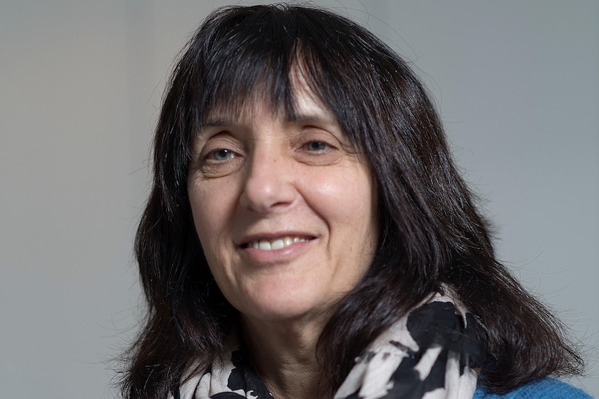 Cathy Kezelman wears a blue jumper and black and white scarf in front of a grey background