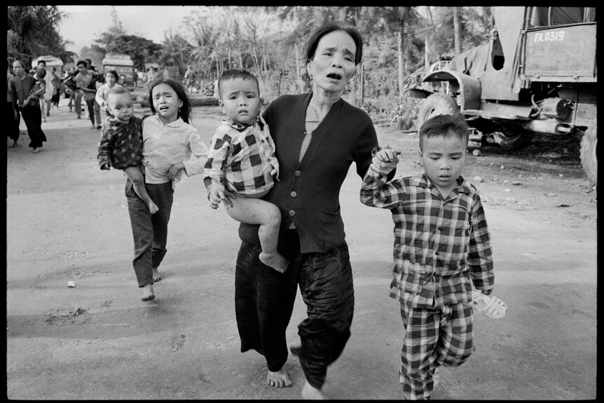 A B&W image of a mother and her children in distress running down the street.