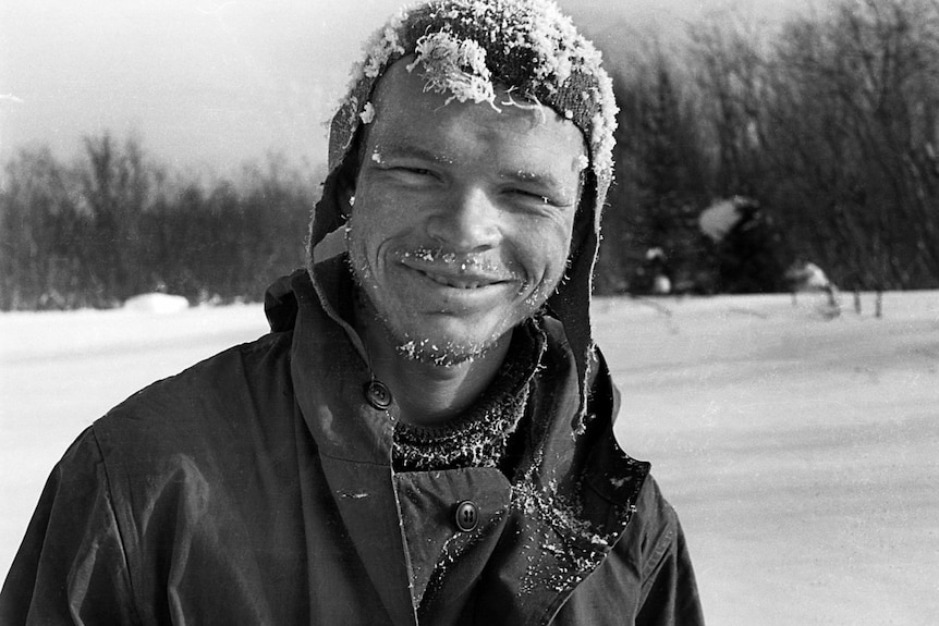 A black and white photo of a young man with snow in his beard and on his beanie
