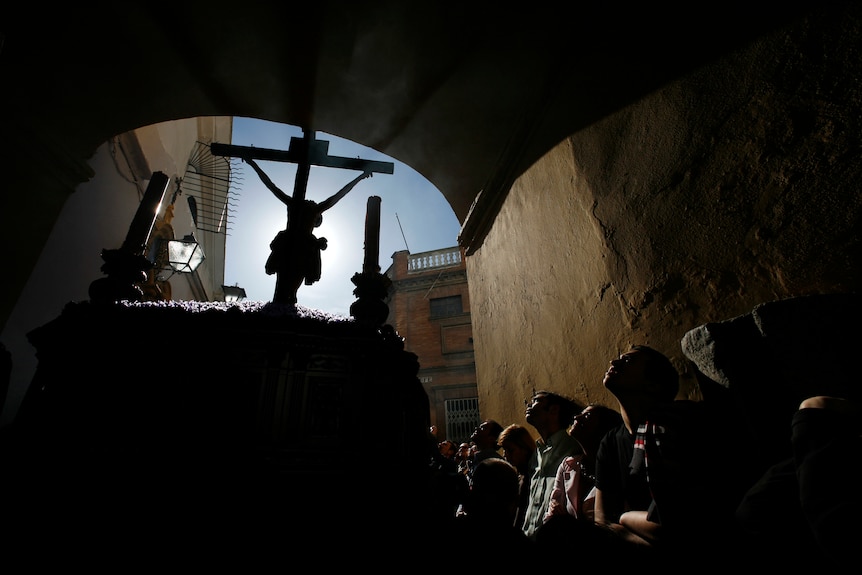 A line of people in a tunnel look up at a crucifix carried in a procession.