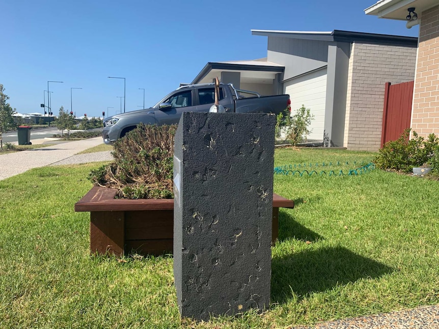 A close up photo of a letterbox in a new housing estate. The letterbox has many dints in it.