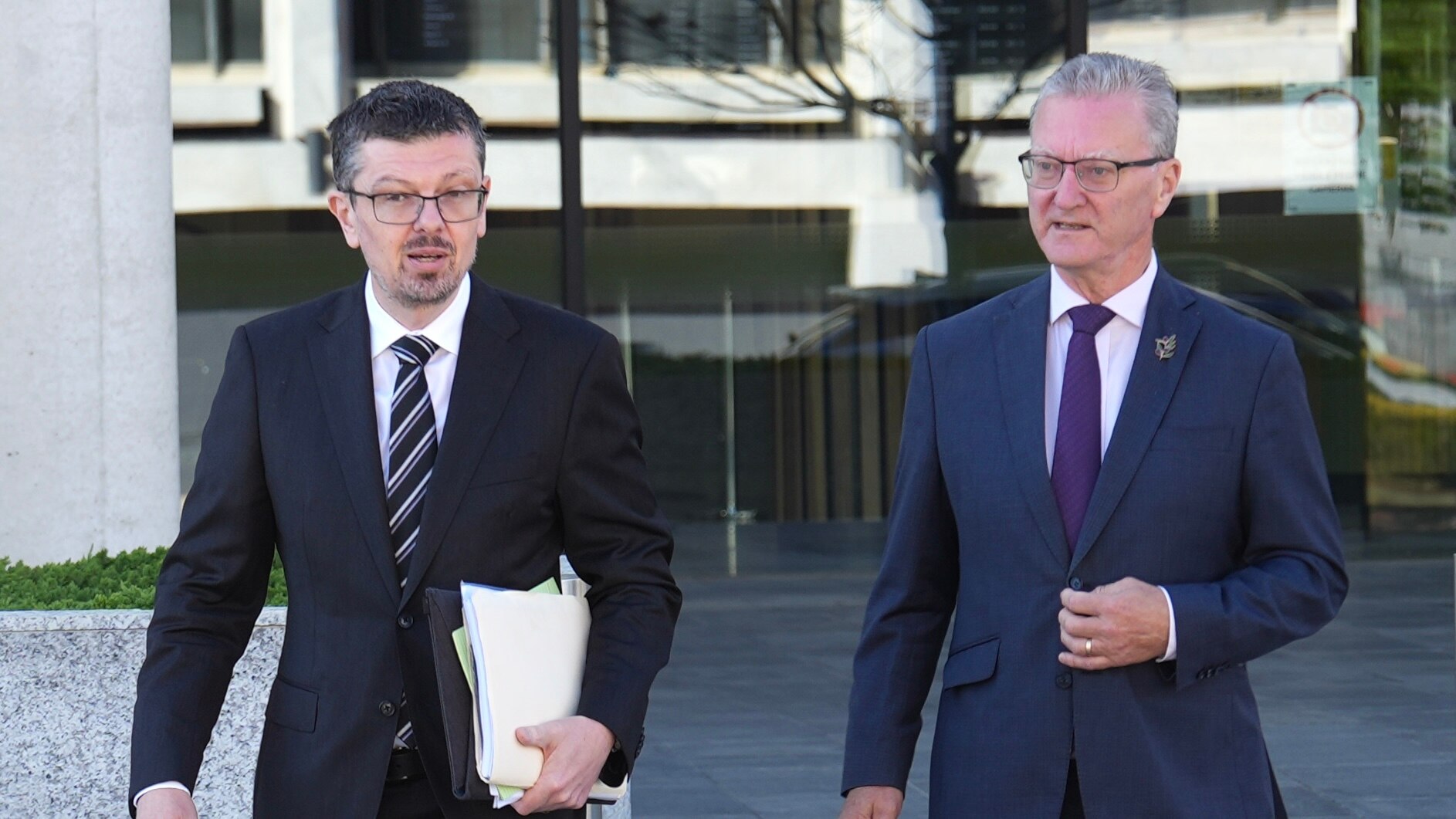 Two men in suits walk outside building.