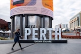 A woman wearing a face mask walks past the Yagan Square sign in Perth's CBD.