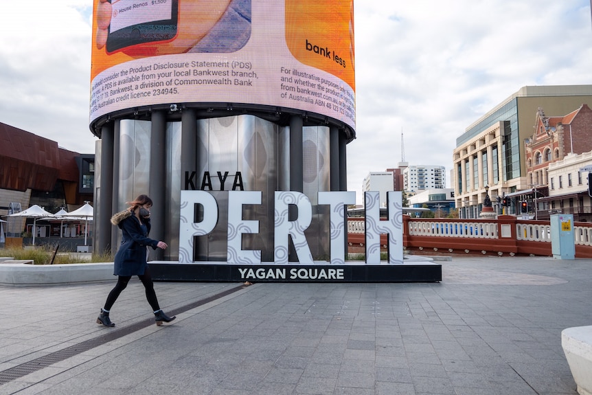 A woman wearing a face mask walks past the Yagan Square sign in Perth's CBD.