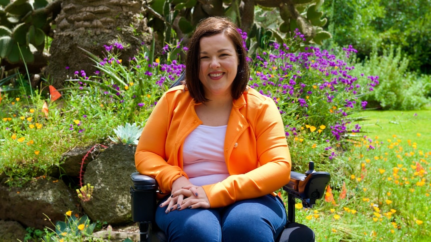 Woman who is brightly dressed smiles as she sits in a flower garden