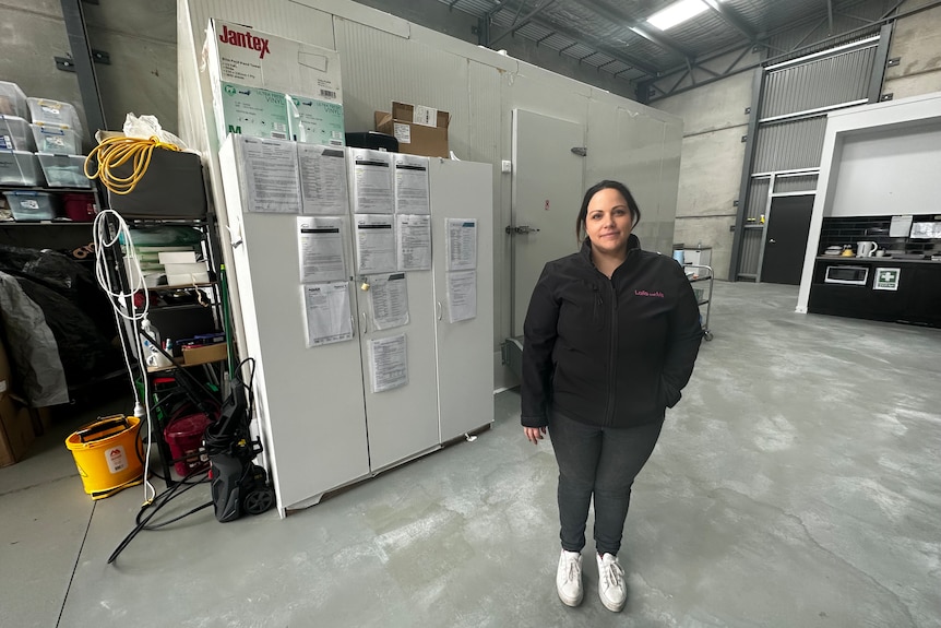 woman standing inside a factory in front of a big commercial fridge.