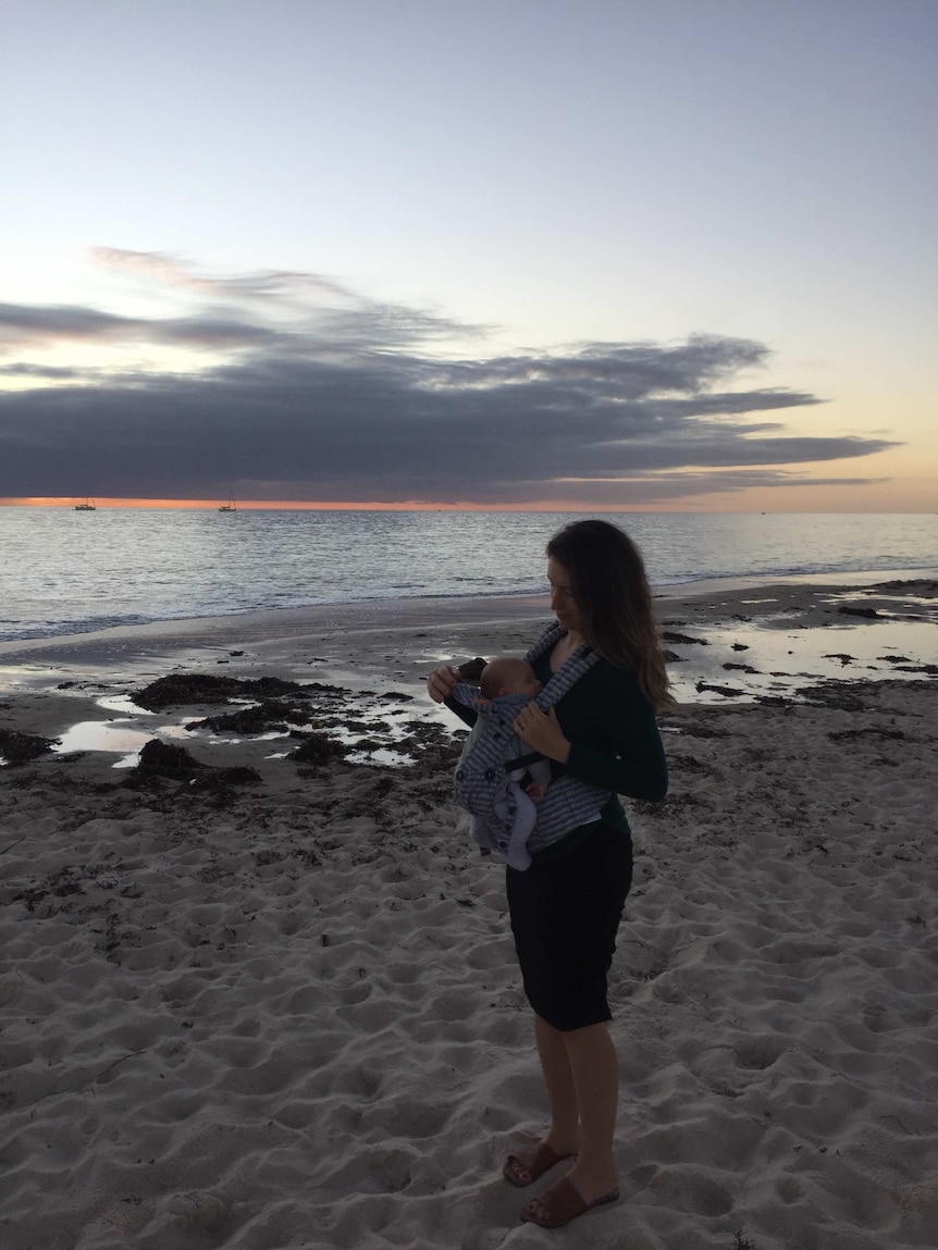 A woman holds a baby on the beach