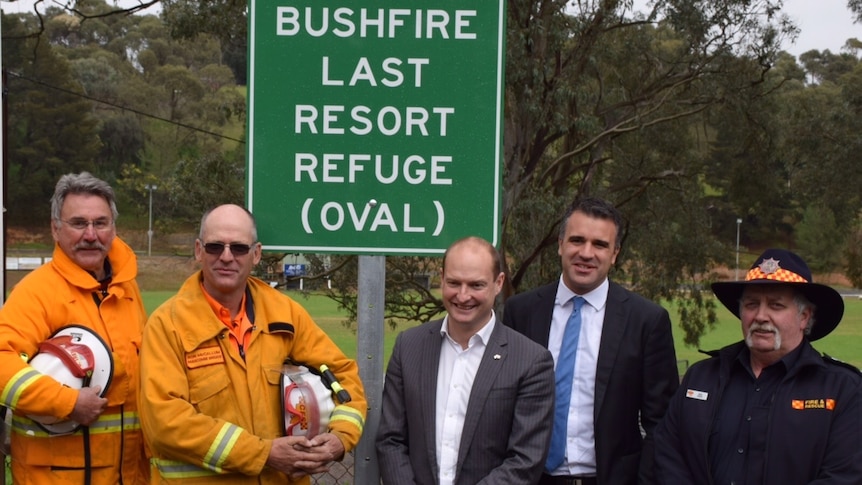 Officials standing in front of a bushfire warning sign