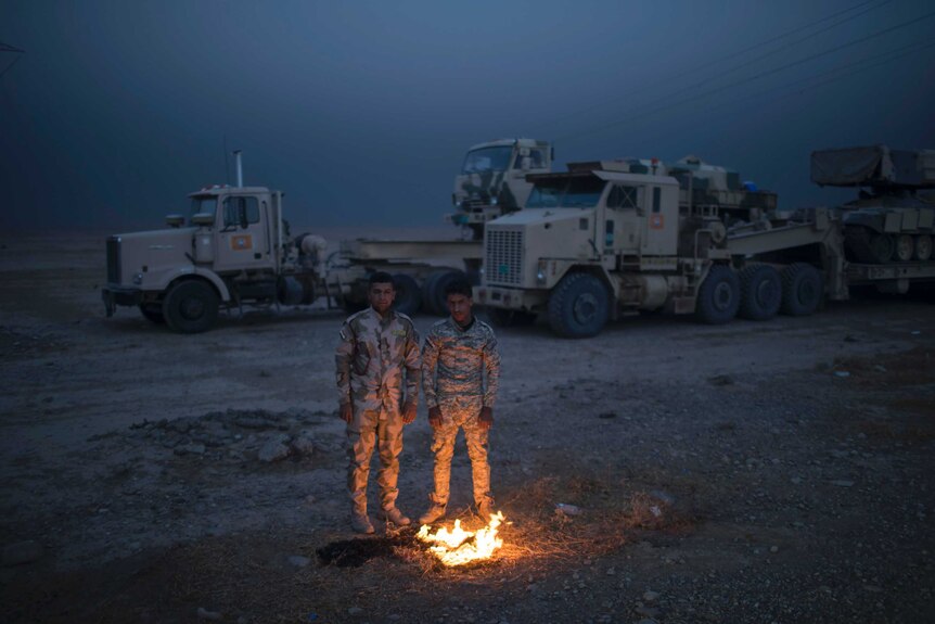 Iraqi army soldiers warm themselves next to a fire near the Qayara air base.