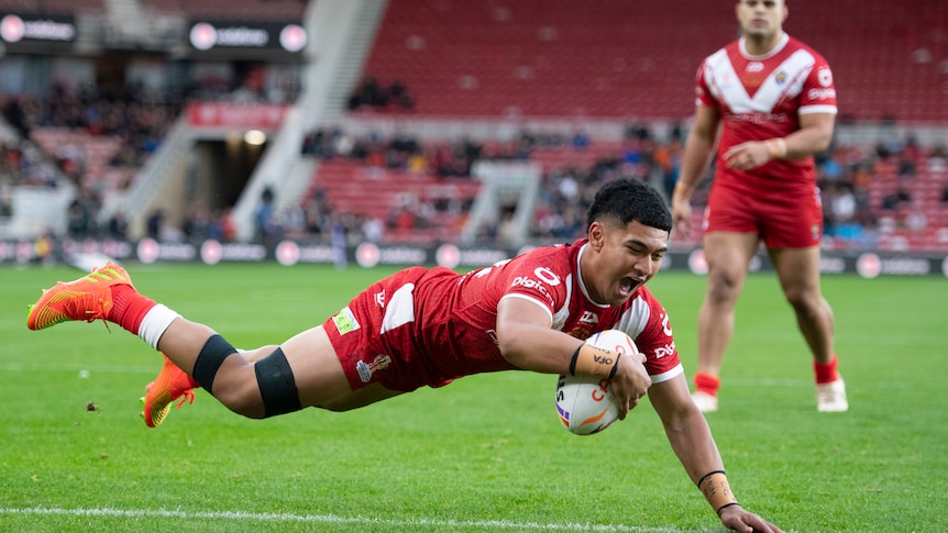 A player dives across the line to score a try in a rugby league match