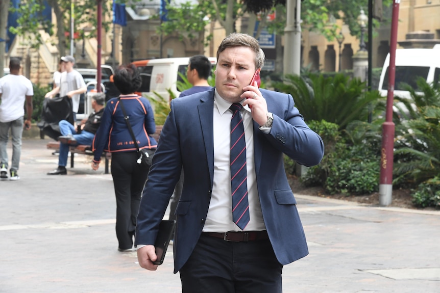 a young man wearing a suit walking outdoors talking into a mobile phone