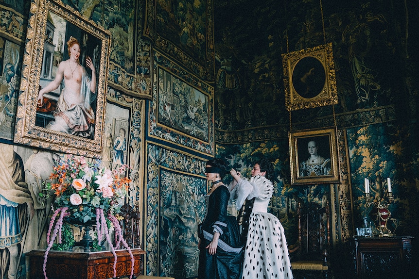 Colour still of Olivia Colman putting a blindfold on Rachel Weisz in 2018 film The Favourite.